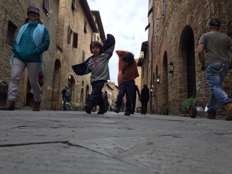 2 kids pretending to be aeroplanes, running down the streets of San Gimignano, Italy